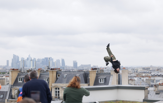 Nathanaël Trier en saut de parkour au-dessus des toits de Paris avec La Défense en fond